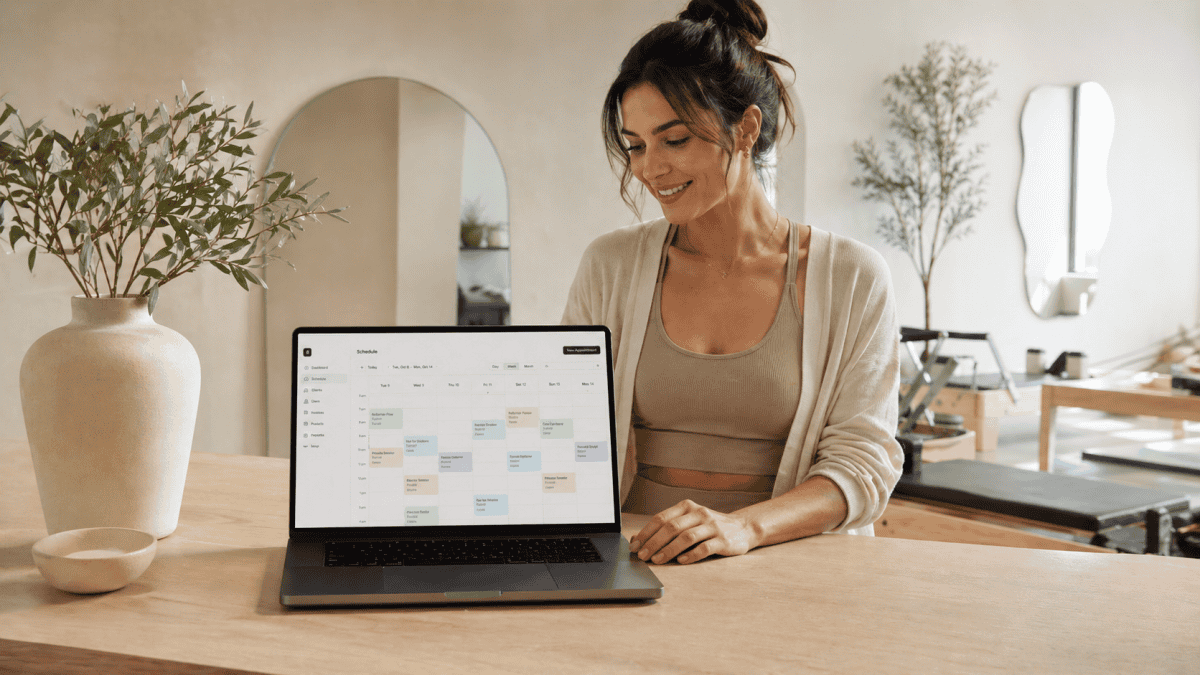 A Pilates studio owner in a studio with a laptop in the foreground showing the calendar view of her studio software